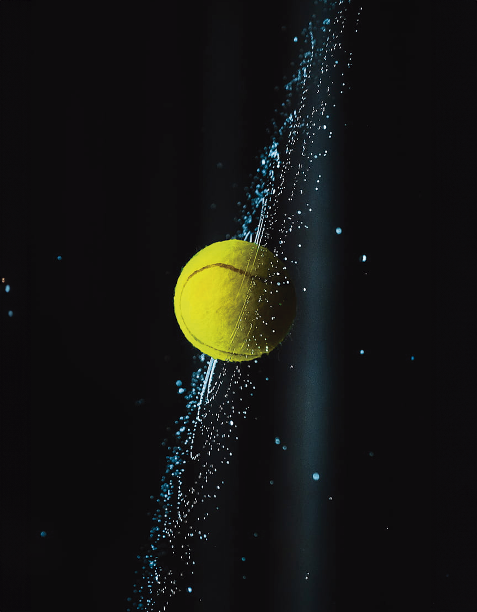 Pelota de tenis flotando en un espacio oscuro, rodeada de partículas brillantes en azul, dando un efecto cósmico moderno. Ideal para decorar.